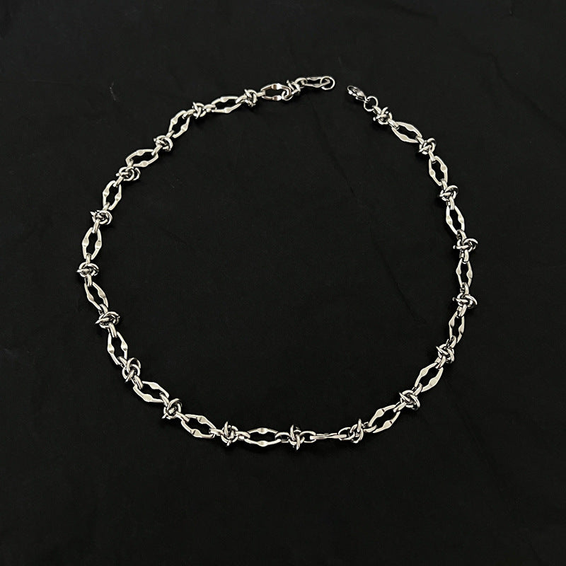 Silver barbed wire necklace with twisted chain laid flat on black background.