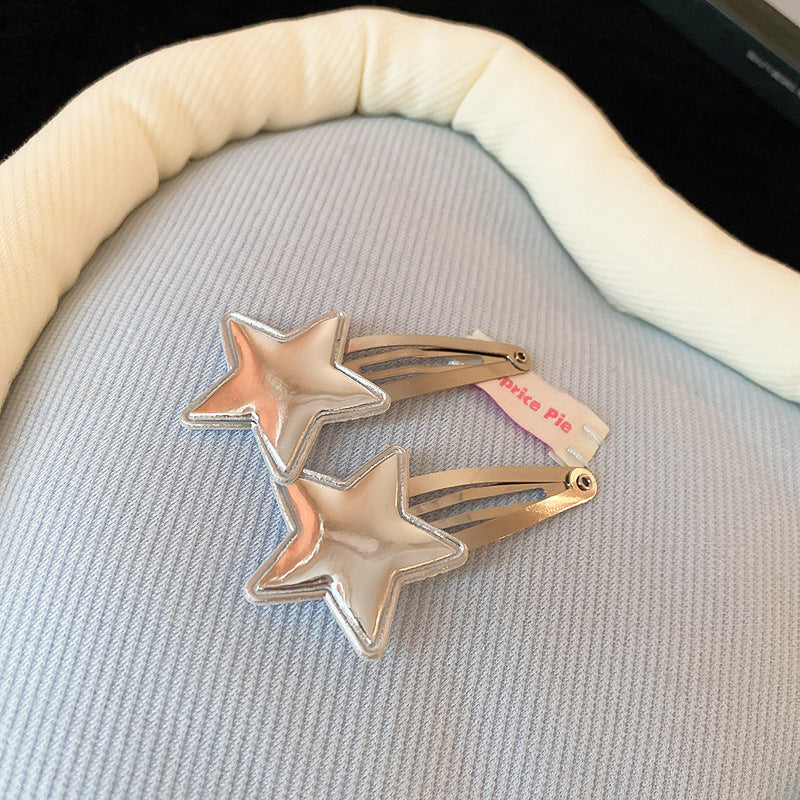 Metallic silver star snap hair clips with a glossy finish, displayed on soft fabric.