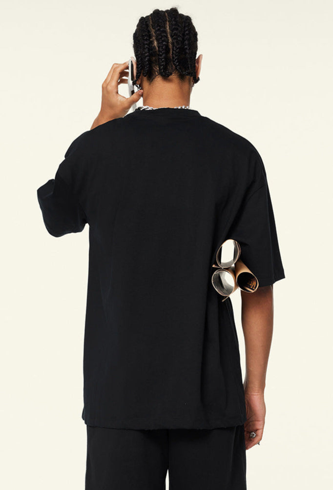 Back of black oversized T-shirt worn by model with rolled posters under arm.