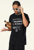 Model wearing black graphic tee talking on phone, holding rolled posters under arm.