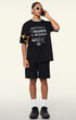 Model in black oversized graphic tee and shorts holding posters and talking on phone.