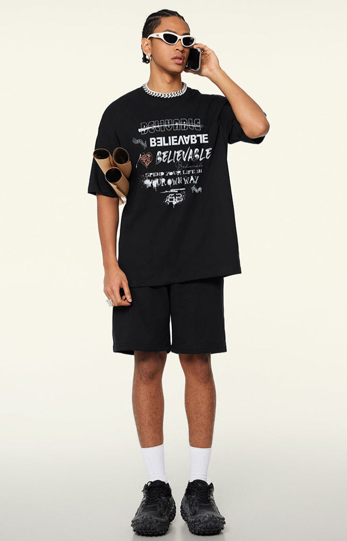 Model in black oversized graphic tee and shorts holding posters and talking on phone.