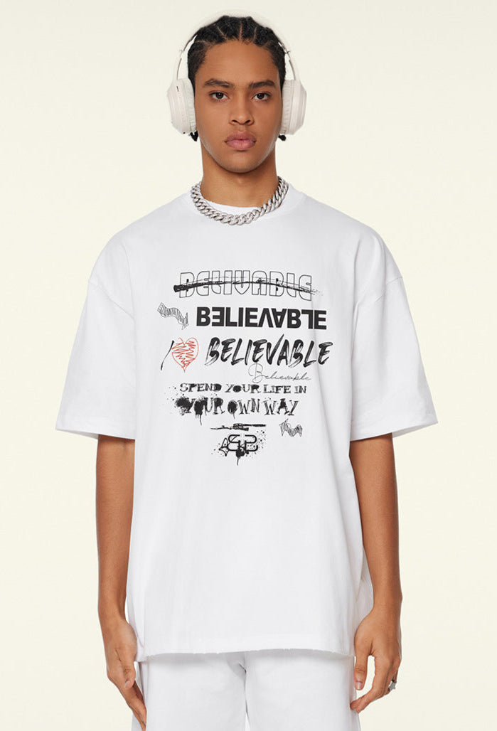 Model facing forward in white oversized tee with layered 'Believable' typography print.