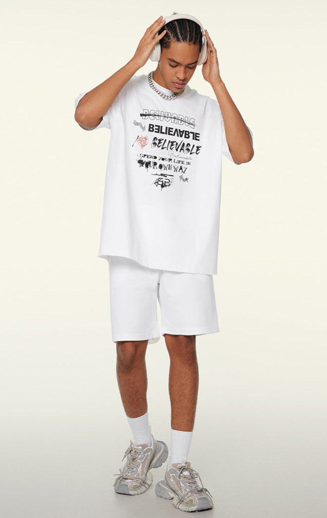 Model wearing white oversized graphic tee and shorts, looking down while adjusting headphones.