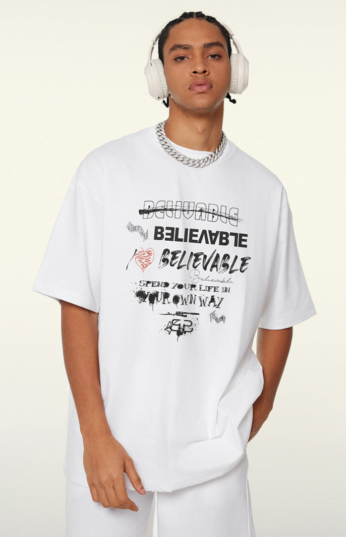 Model in white graphic tee posing with hand in pocket and wearing headphones.