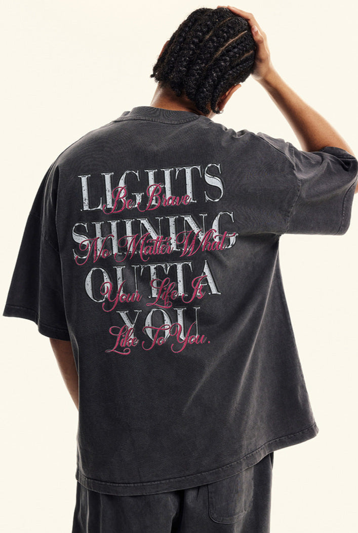 Back of black tee with layered street-style typography reading 'Lights Shining Outta You.