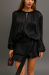 Close up of woman in a black chiffon ruffle set holding a small handbag against a gray background