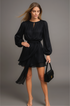 Woman wearing a black ruffle set holding a matching handbag against a gray background