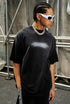 Man in black gradient quote tee wearing sunglasses while posing against industrial backdrop.