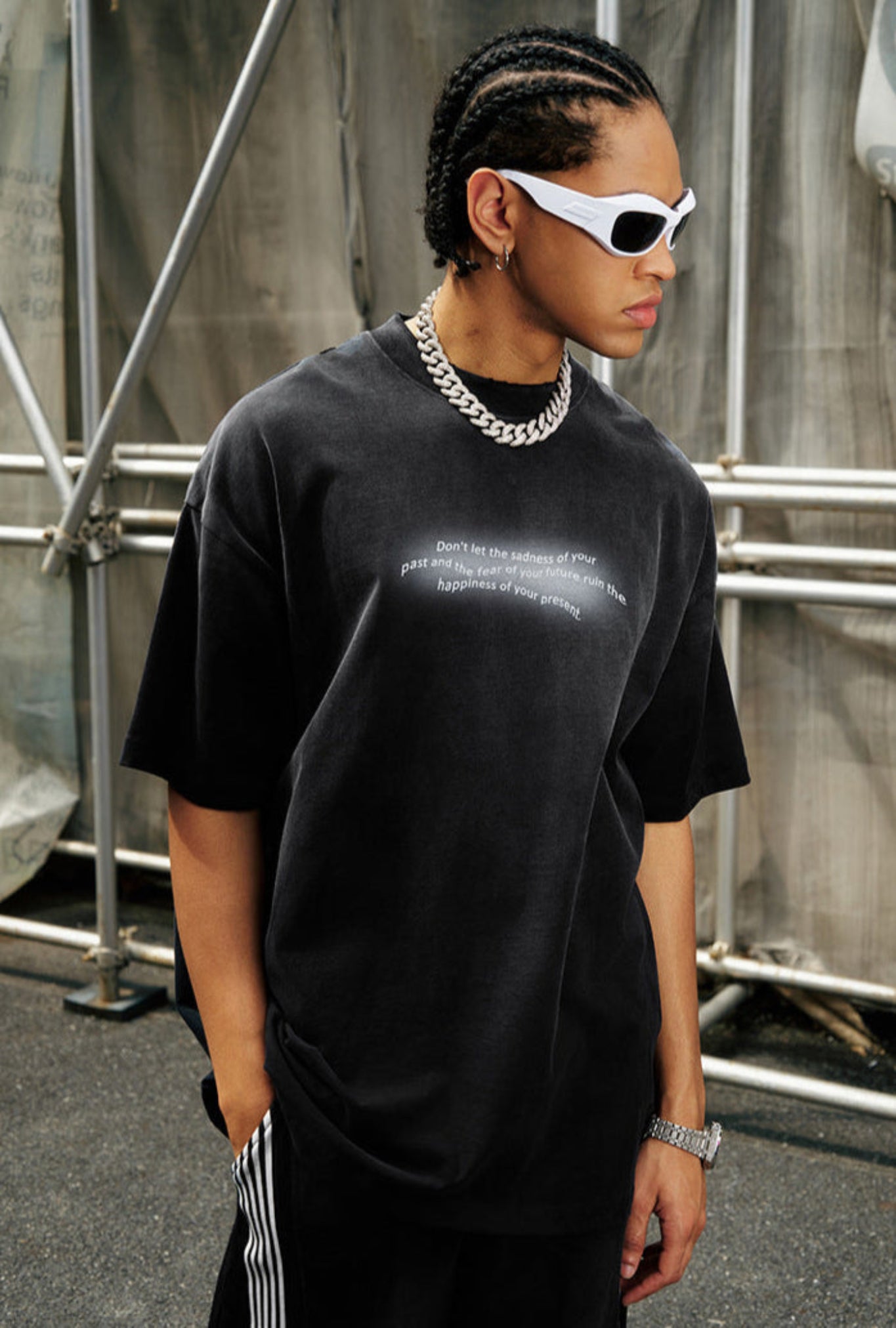 Man in black gradient quote tee wearing sunglasses while posing against industrial backdrop.