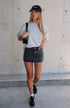 Model wearing a grey oversized t-shirt, black washed denim mini skirt, sneakers, and a black baseball cap.”