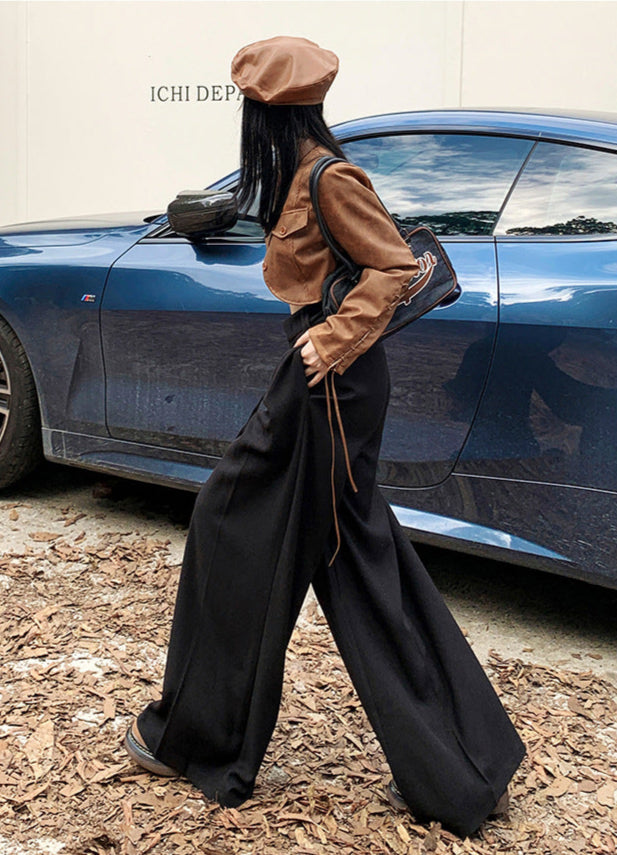 Side profile of model walking in black wide-leg trousers with high waist and soft drape.