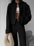Person wearing a lounge set with black jacket and pants holding a beige bag indoors.