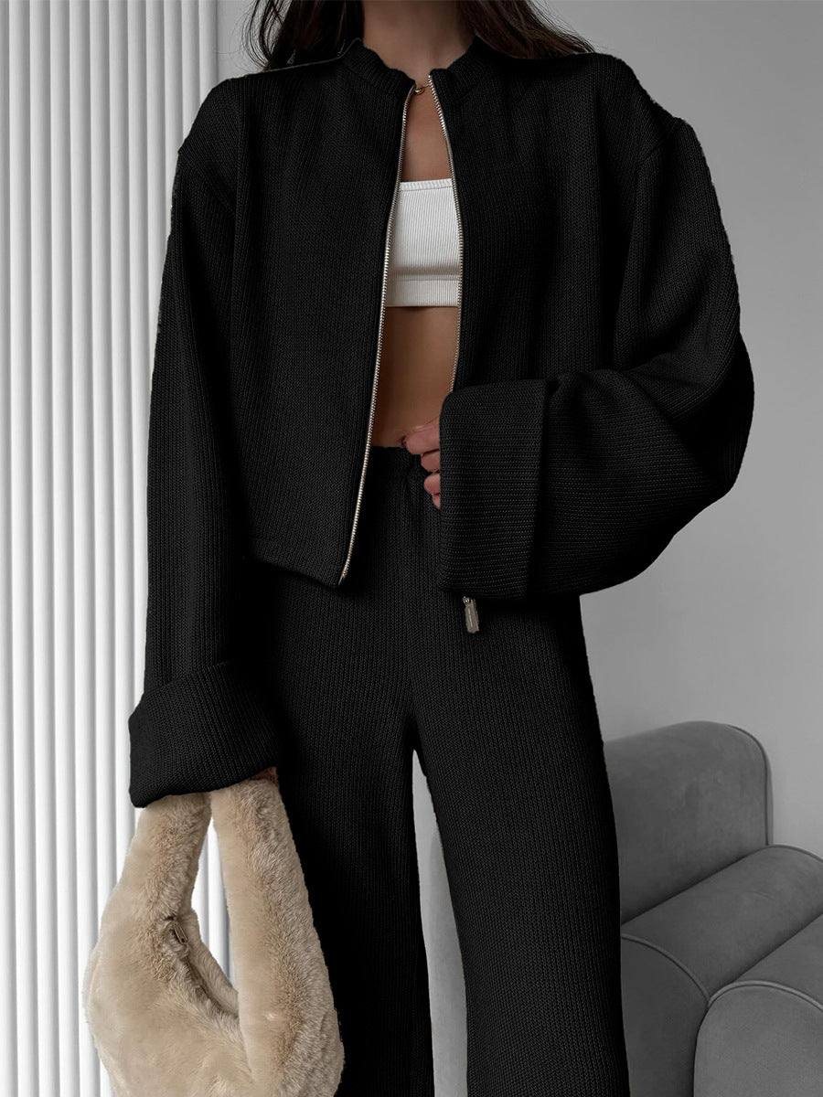 Person wearing a lounge set with black jacket and pants holding a beige bag indoors.
