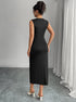 Back view of woman wearing a black sleeveless slit dress standing in a room with gray walls and white curtains.