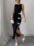 Woman wearing a black slit dress with white bow details, holding a small white handbag, against a plain background.