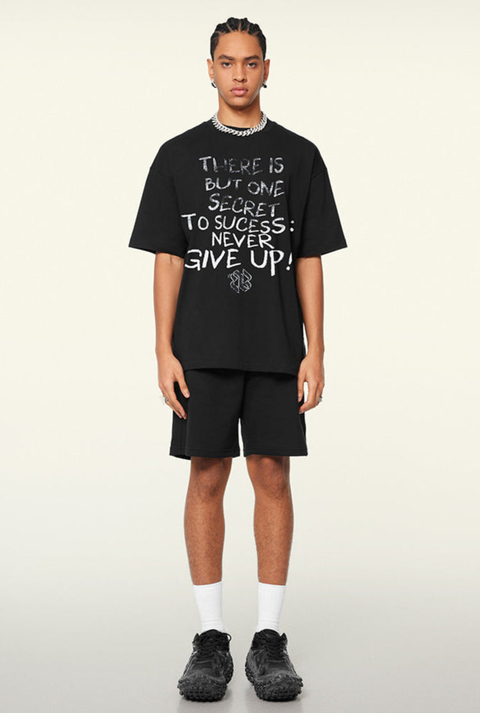 Male model in black oversized T-shirt and shorts with motivational quote, standing in neutral pose.