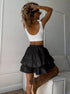 Back view of woman in a white crop top and black ruffled polka dot skort, hand in her curly hair.