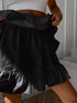 Close-up of woman wearing a white ribbed crop top and lifting the ruffled layers of a black polka dot cotton mini skort.
