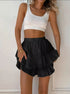 Front view of woman in a white ribbed crop top and black ruffled polka dot mini skort, lightly holding the hem.