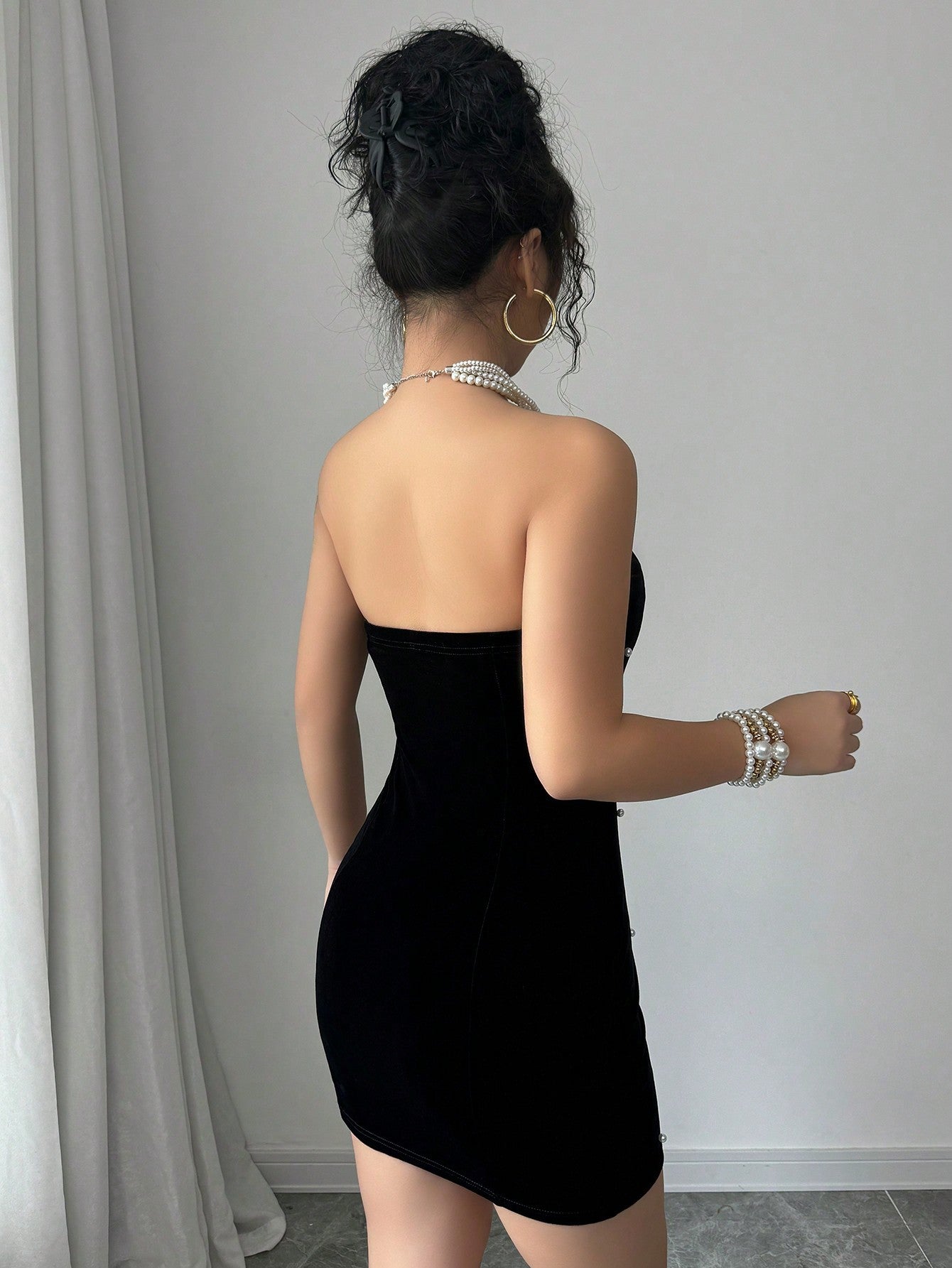 Back view of black velvet bodycon mini dress with smooth strapless design and hip-hugging fit.