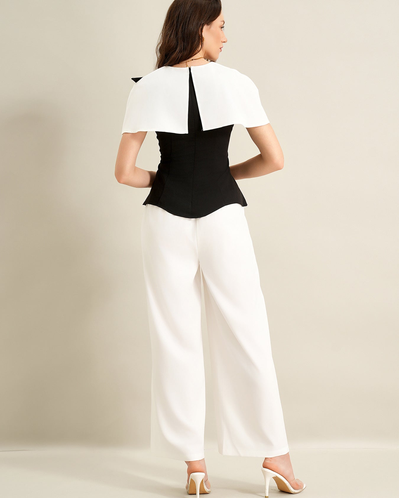 back view of woman wearing black cape top and white trousers