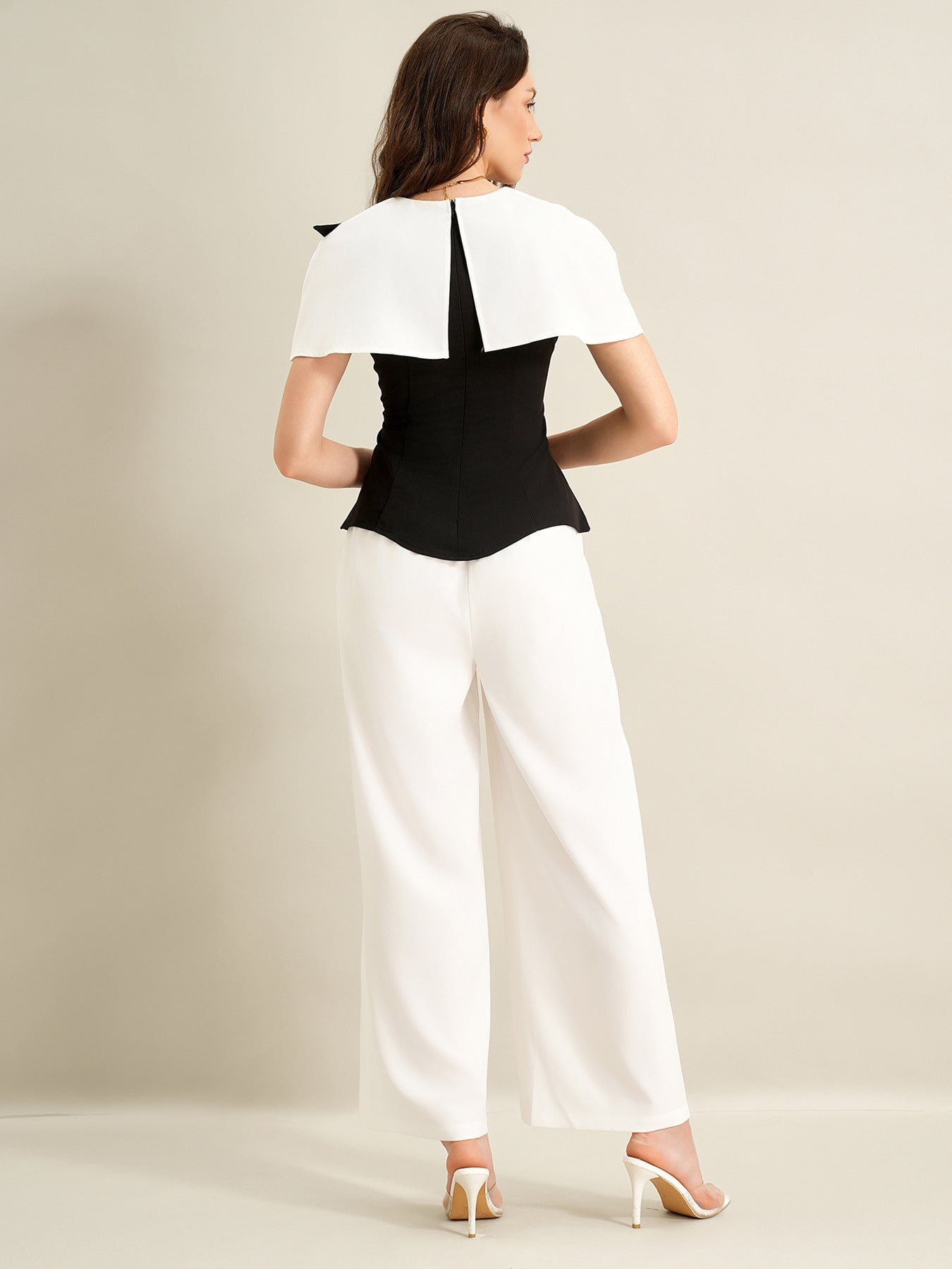 back view of woman wearing black cape top and white trousers