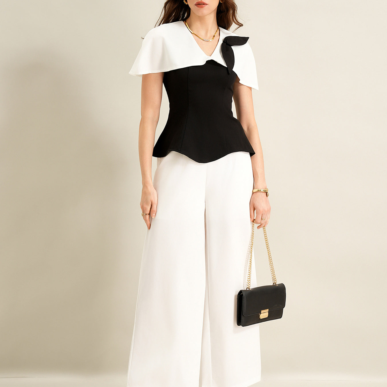 woman wearing black cape top and white wide leg trousers holding black handbag