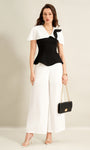 woman wearing black cape top and white wide leg trousers holding black handbag
