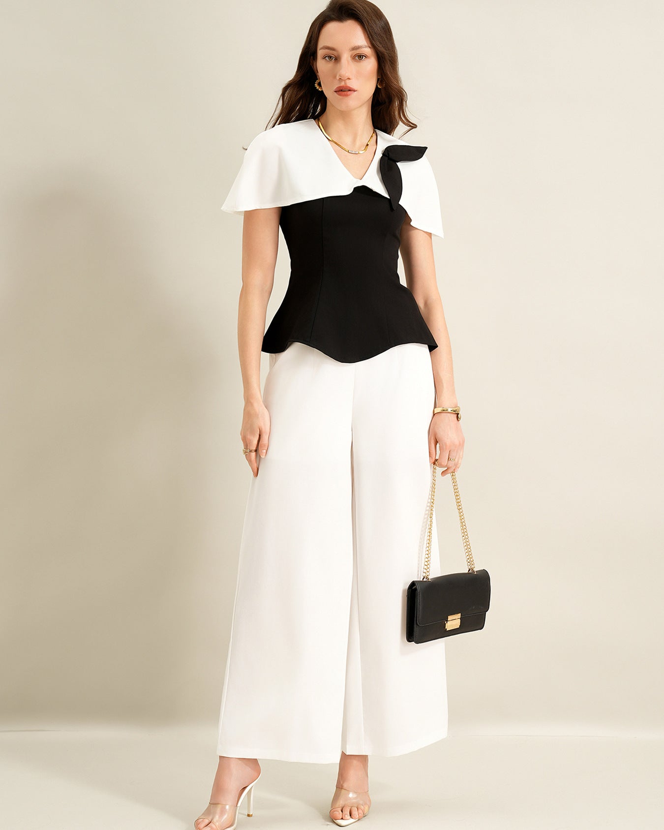 woman wearing black cape top and white wide leg trousers holding black handbag