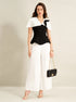 woman wearing black cape top and white wide leg trousers holding black handbag