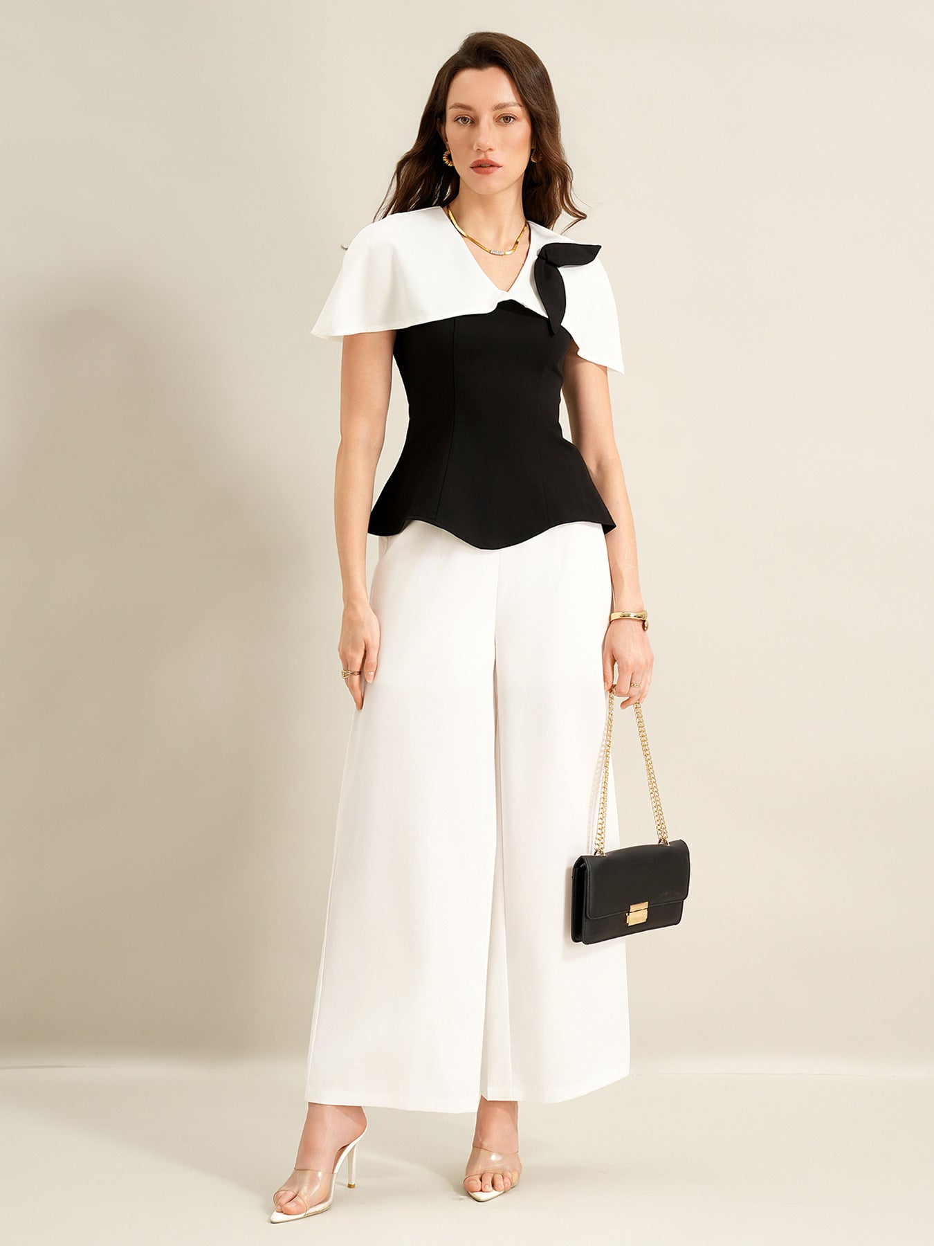 woman wearing black cape top and white wide leg trousers holding black handbag