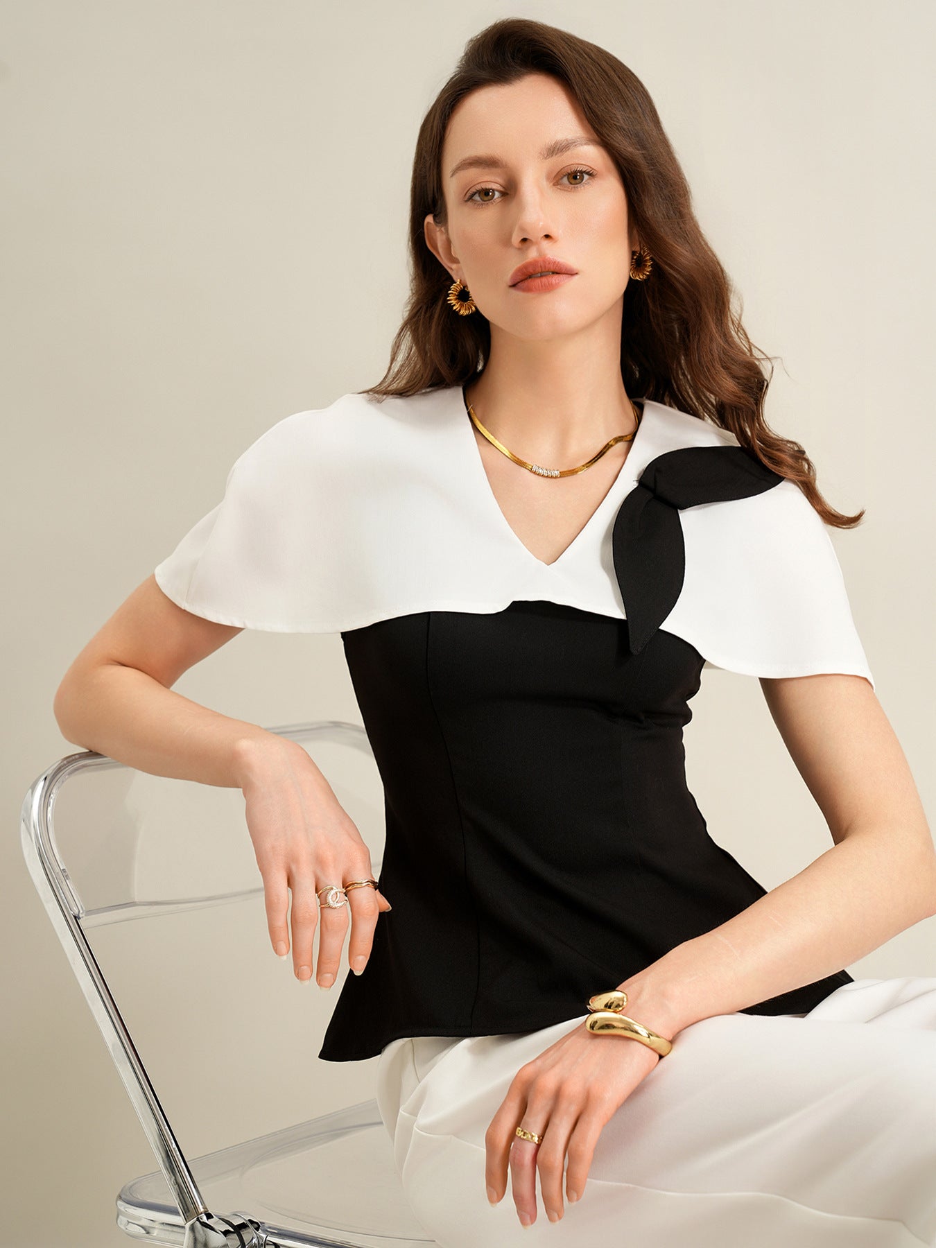 woman seated wearing black cape top and white trousers