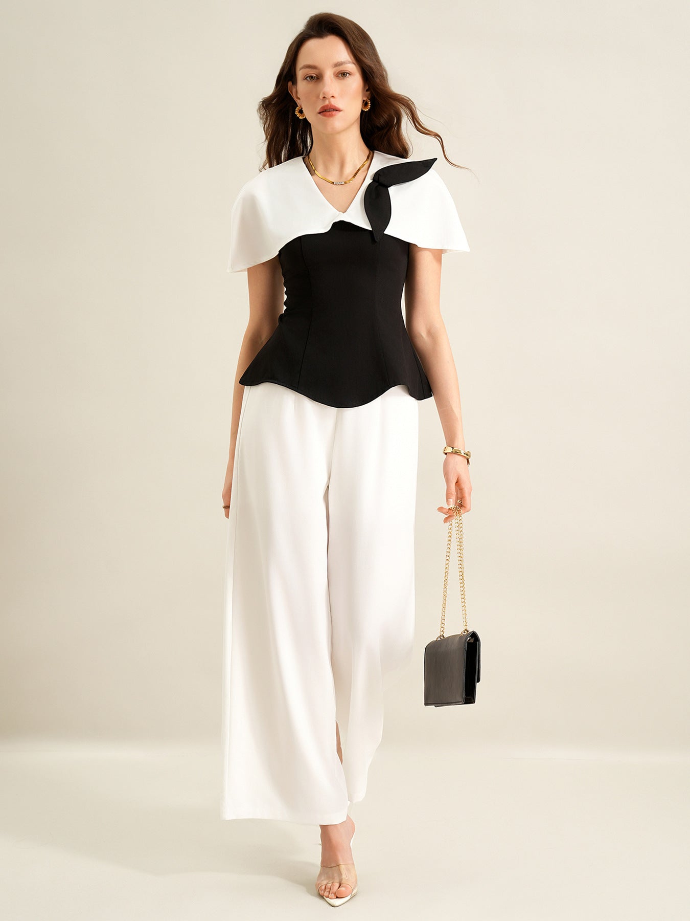 woman walking wearing black cape top and white trousers holding small bag