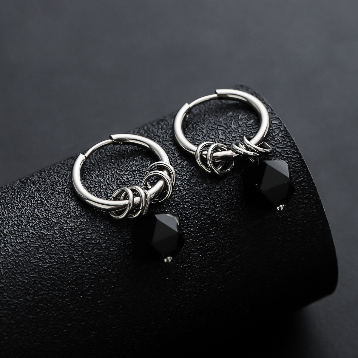 Pair of silver hoop earrings with black zircon charms on textured display.