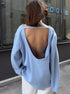 Person wearing a light blue sweater with an open back, standing on a street.