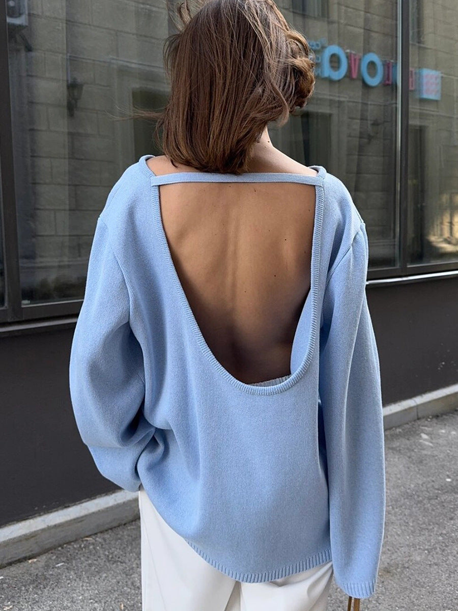 Person wearing a light blue sweater with an open back, standing on a street.