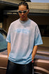 Close-up of man in blue gradient tee and chain necklace, looking forward with hands in pocket.