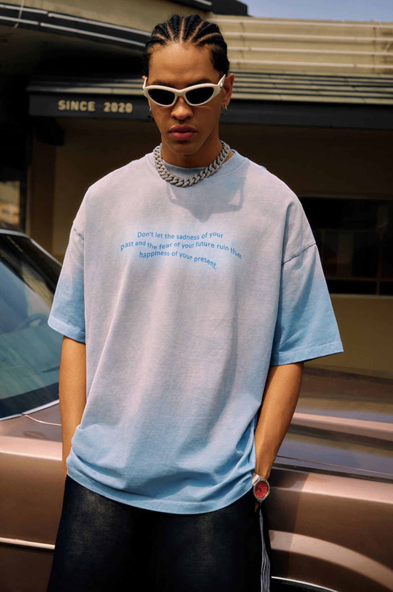 Close-up of man in blue gradient tee and chain necklace, looking forward with hands in pocket.