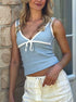 Woman wearing slim-fit blue knit cami with lace trim and bow detail, paired with cream drawstring pants.
