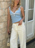 Full-body view of woman in blue cami tank with lace bow trim and wide-leg cream pants holding a small purse.