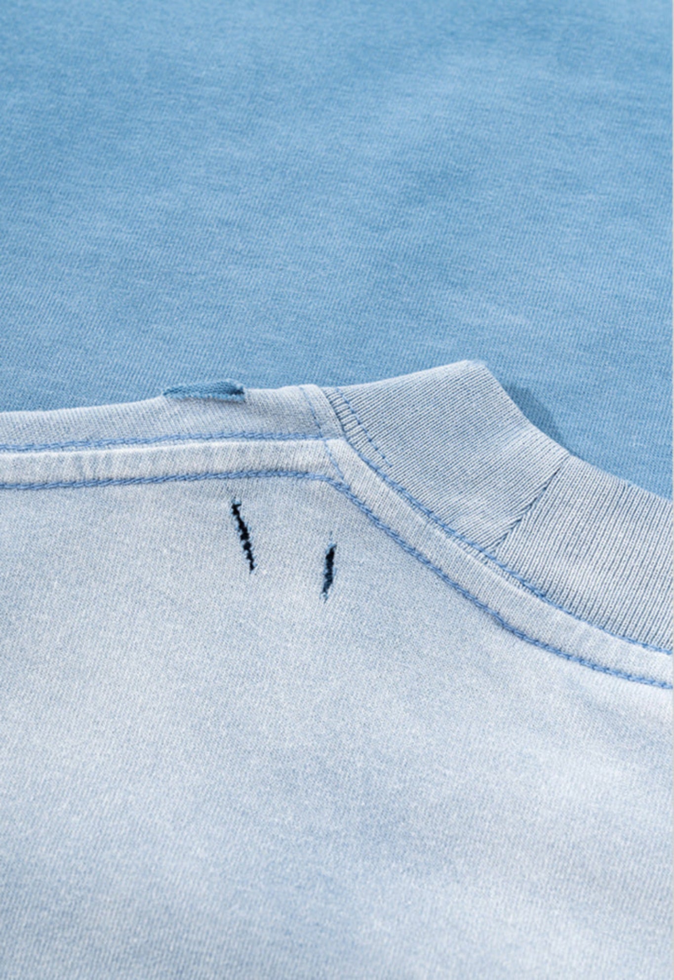 Close-up of distressed neckline detail on blue tee with contrast wash.