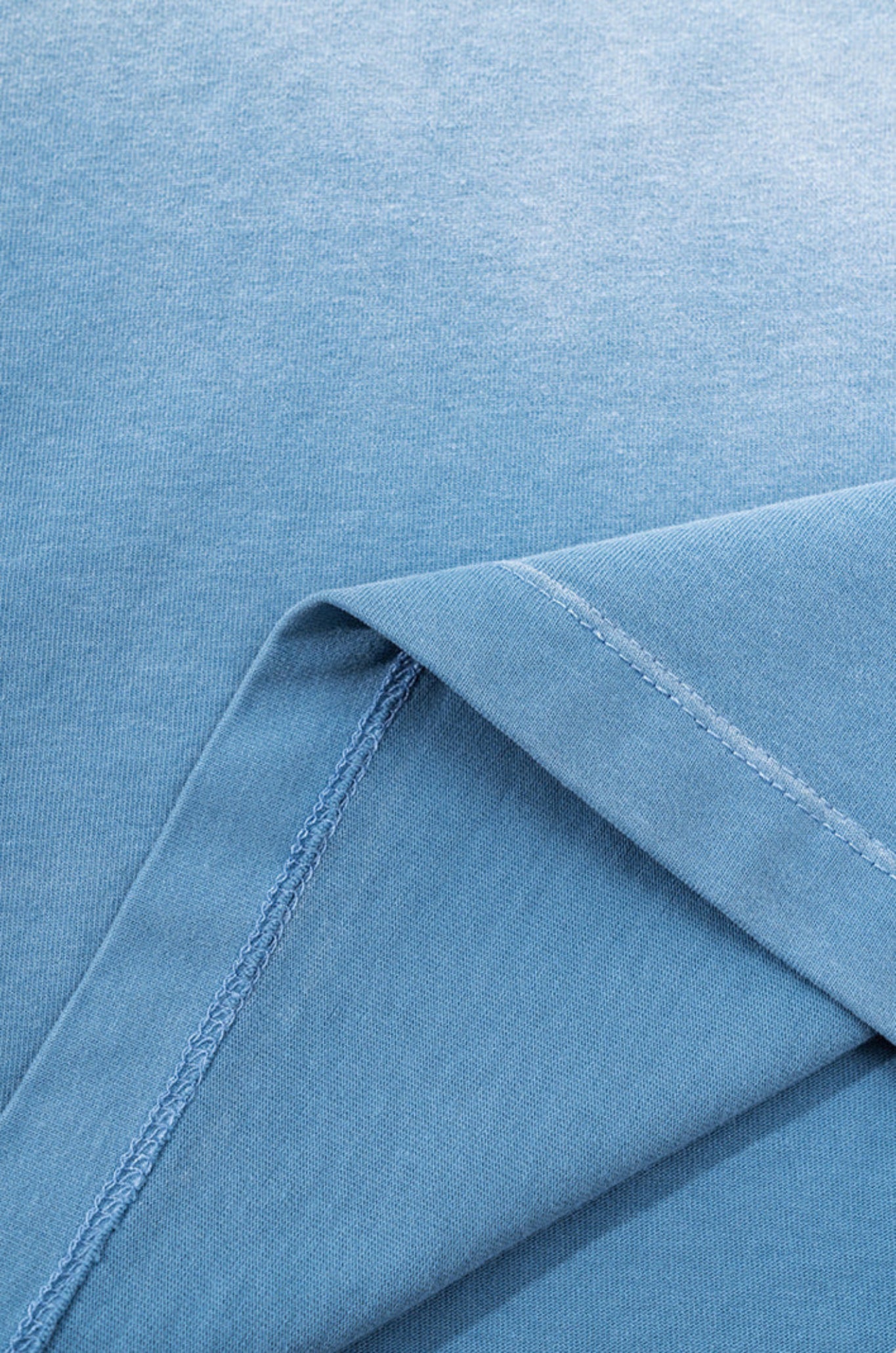 Close-up of inside seam and hem stitching on blue gradient tee fabric.