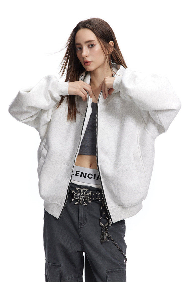 Front view of a model wearing a heather light grey boxy zip up hoodie open over a grey tank top and dark jeans.