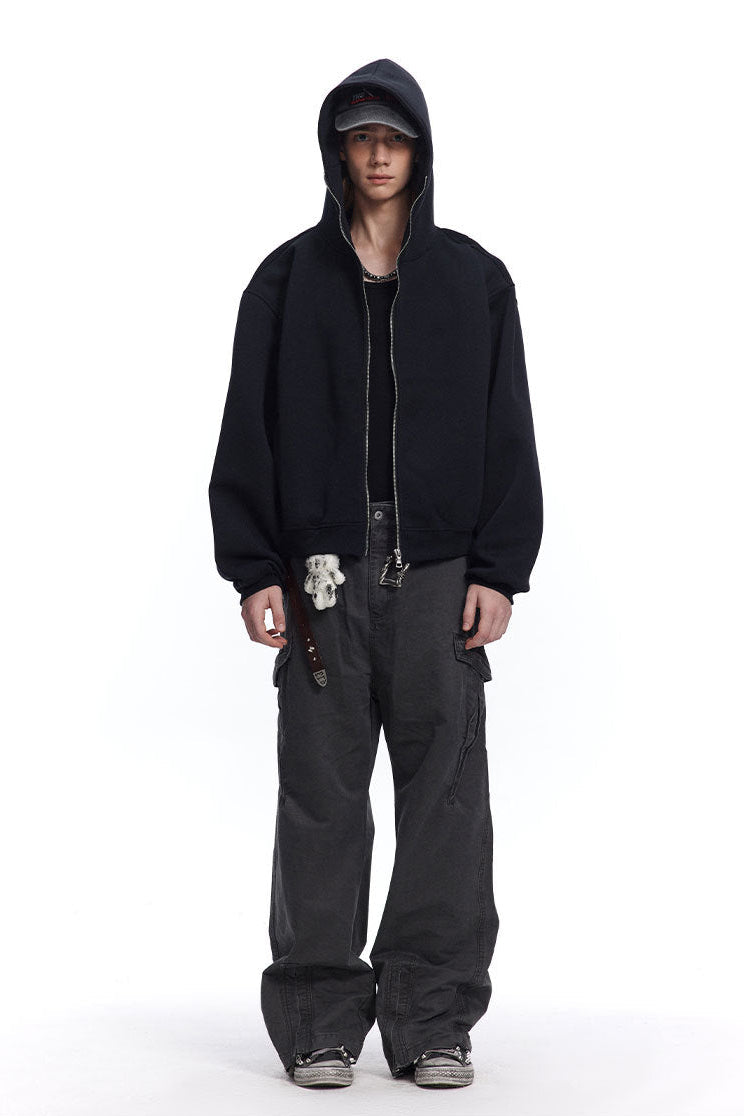 Front full body shot of a male model wearing a black full-zip oversized hoodie jacket with hood up.