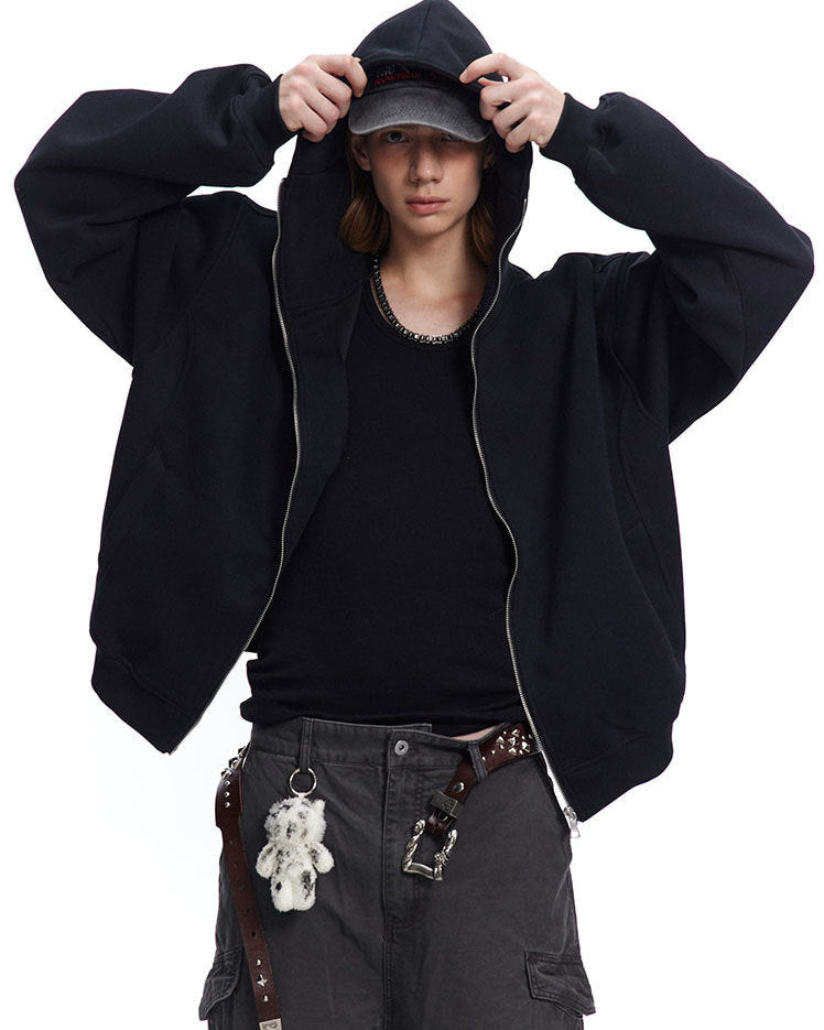 Medium shot of a male model adjusting cap while wearing a black boxy fit zip up hoodie.