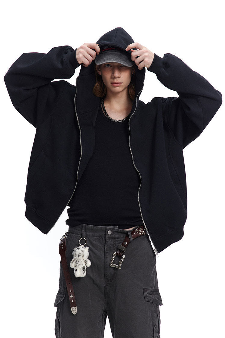 Medium shot of a male model adjusting cap while wearing a black boxy fit zip up hoodie.
