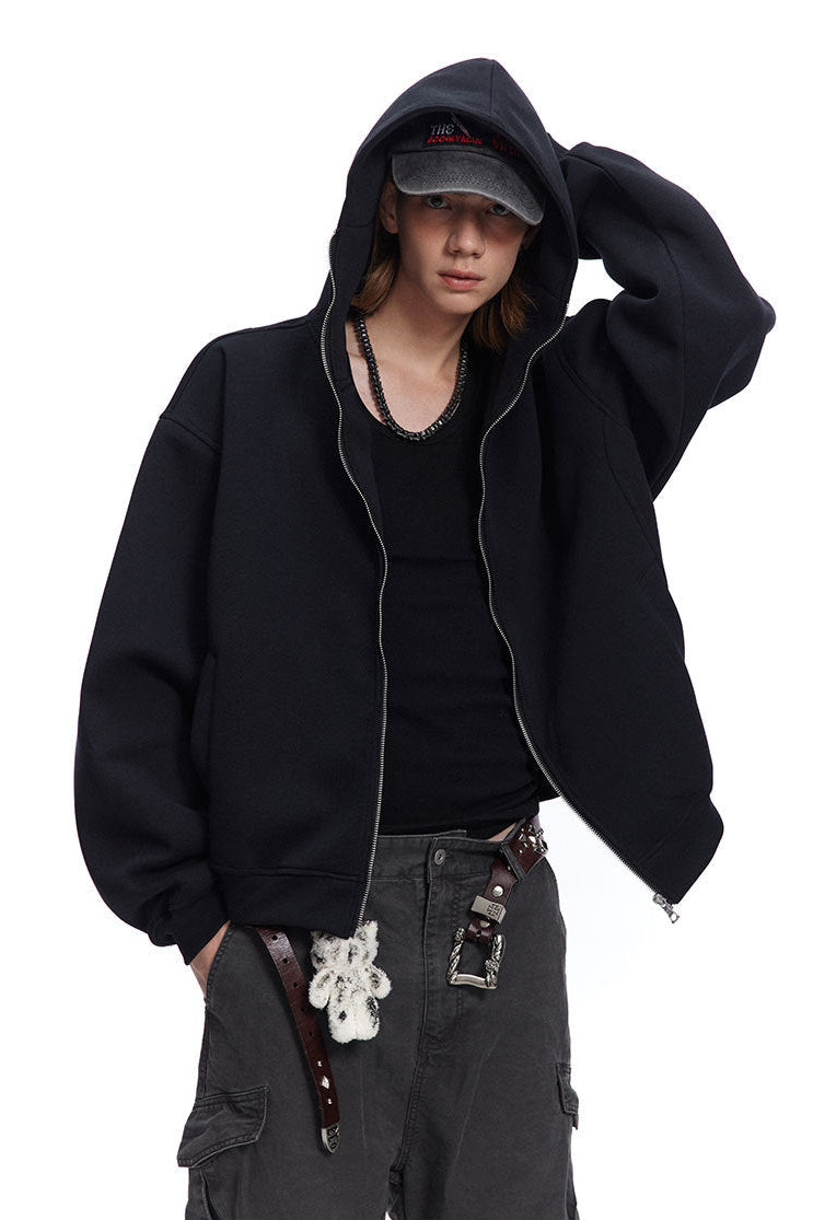 Three-quarter view of a male model wearing a black relaxed fit hooded zip jacket.