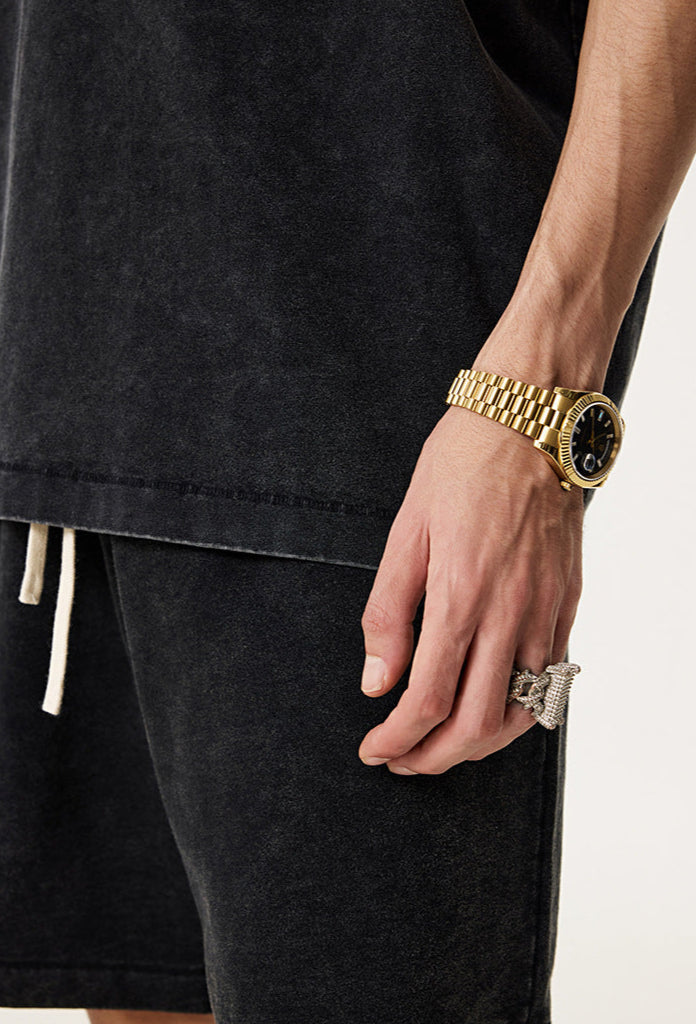 Close-up of hand wearing gold watch and ring, styled with vintage black tee.