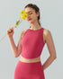 Woman in brick red high-neck crop top and leggings holding a yellow flower to her face.